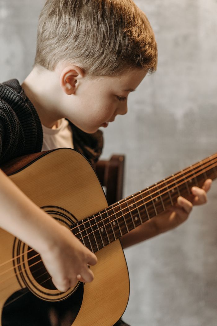 our-experience Child practicing guitar chords, focused indoors on musical growth.