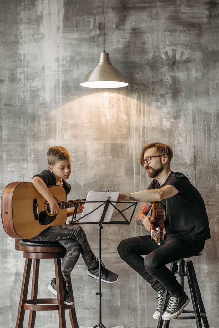services-img Teacher and young boy in guitar lesson, under modern lighting, indoors.