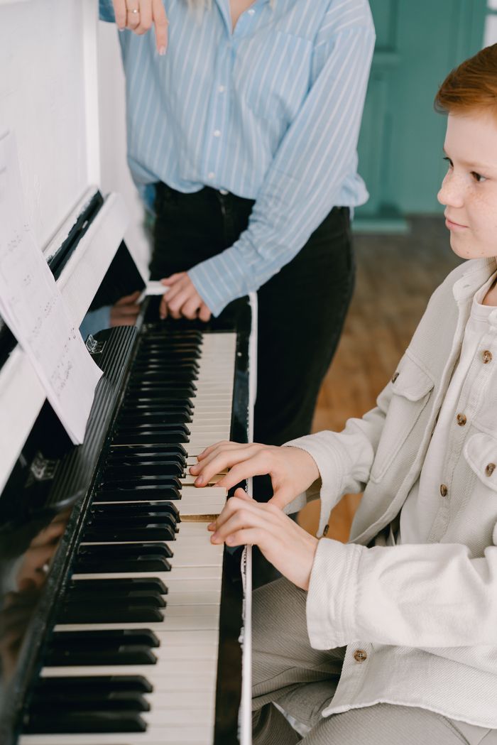 about-02 Child practicing piano under guidance of instructor indoors.