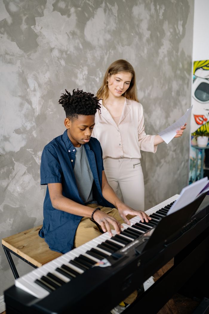 ours-journey A young boy receives piano lessons from a teacher in a cozy home setting, focusing on music learning.