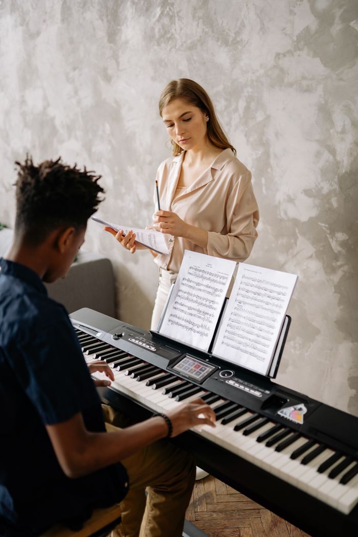 services-01 A young student receiving piano lessons from a teacher, focusing on music sheets.